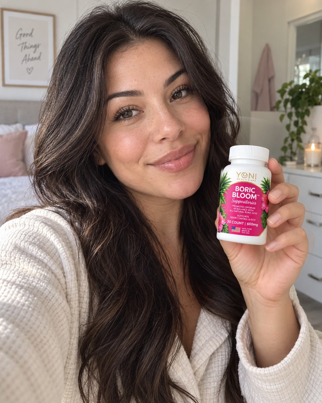 Woman in a cream sweater holding a bottle of Yoni Peach Care Boric Bloom 600 mg suppositories in her bedroom