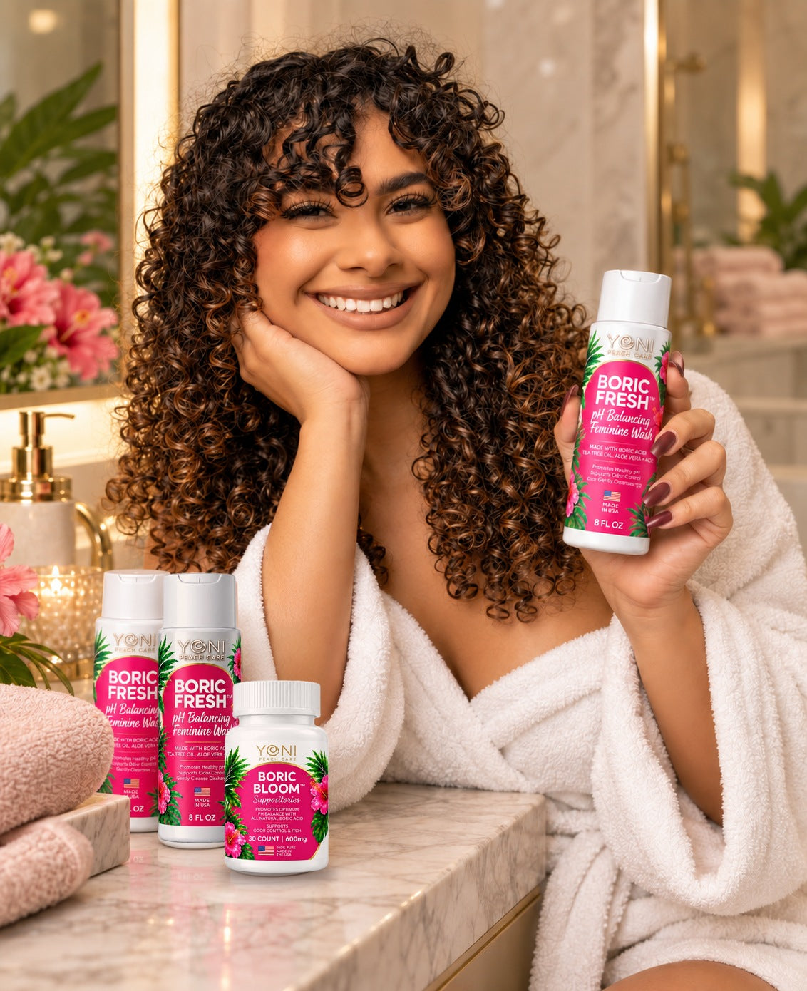 Smiling woman in a white robe holding Boric Fresh wash beside two Boric Fresh bottles and Boric Bloom suppositories on a marble vanity