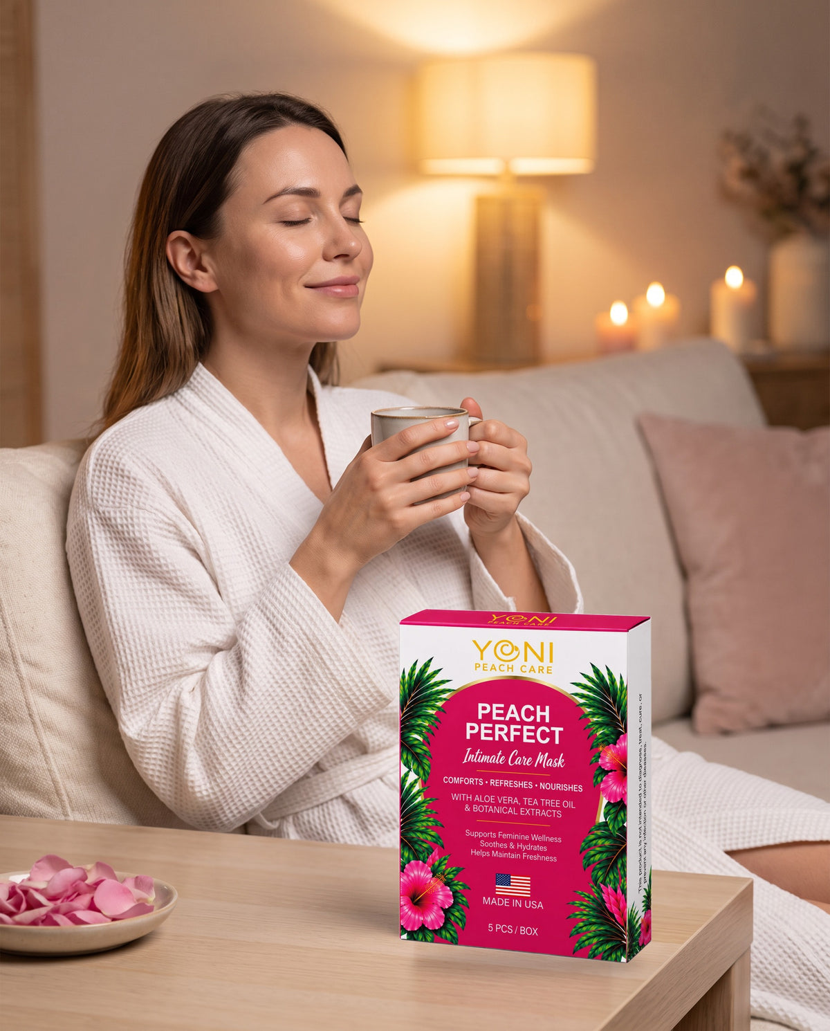 Woman in a white robe relaxing with tea beside the Peach Perfect Intimate Care Mask box on a side table